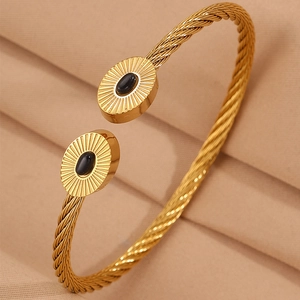 Détail d'un bracelet ouvert torsadé doré avec pierres ovales noires et texture soleil radieux