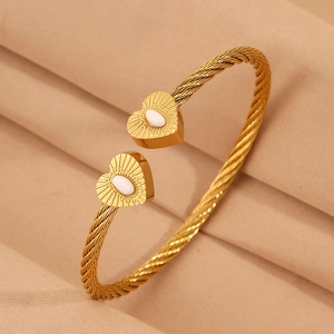 Detail of twisted gold wire open bangle with white shell heart charms in vintage style