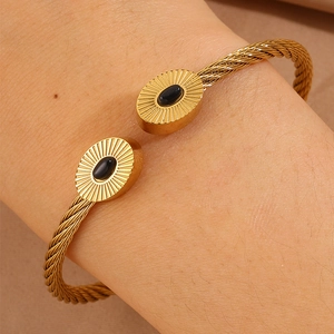 Détail macro du bracelet câble doré avec breloques ovales à motif solaire et pierres noires