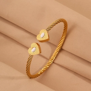 Detail of gold twisted cable bracelet featuring heart charms with white inlay texture