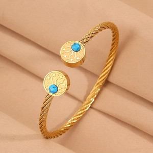 Détail d'un bracelet torsadé doré orné de motifs soleil et étoile avec turquoise bleue