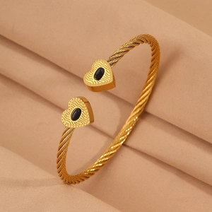 Detailed macro view of golden twisted cable cuff bangle with black heart gemstone