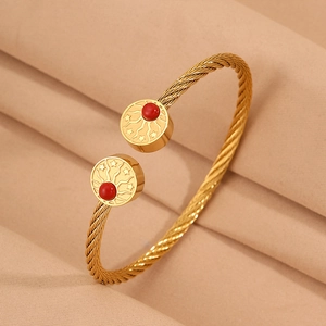 Détail macro du bracelet câble doré avec gravure soleil étoile et perle rouge