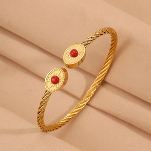 Détail du bracelet rigide en fil d'or torsadé avec perle rouge ovale et gravure rayon de soleil