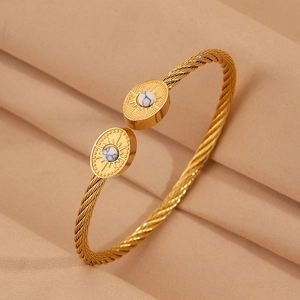 Détail d'un bracelet torsadé doré avec breloques ovales, pierre marbre et gravure de rayons