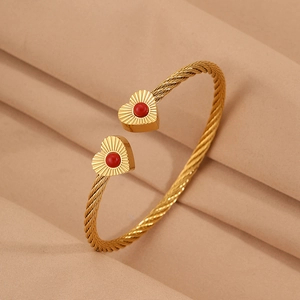 Close-up of golden twisted wire open bangle featuring heart charms with red beads
