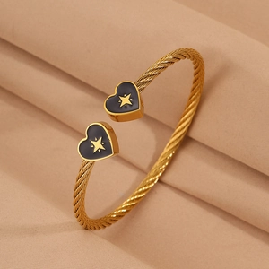 Detailed view of gold twisted wire cuff bracelet with black heart and star charms.