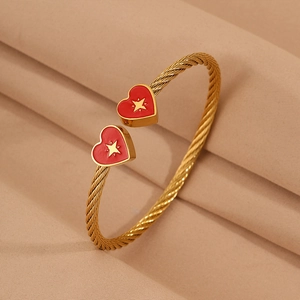 Detail of gold twisted cable bracelet with red enamel heart and star charms on fabric