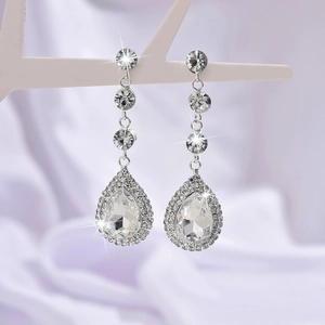 Elegante silberne Tropfenohrringe mit Strass für Bräute auf lila Seidenhintergrund