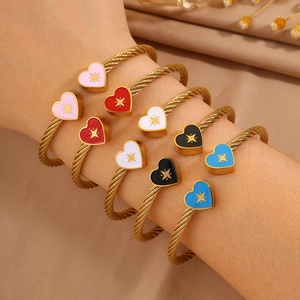 Detail of twisted cable gold bracelets with colorful heart charms and star patterns
