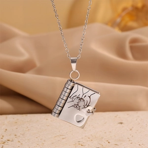 Detailed macro of silver book pendant with hand-in-hand engraving on silk fabric
