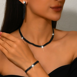 Detailed view of women wearing black rhinestone necklace, bracelet, and long drop earrings set