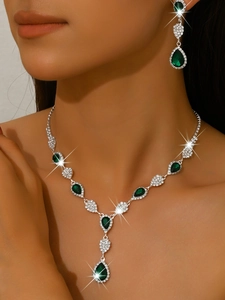 Detailed close-up of emerald green drop necklace and earrings set with crystal rhinestones