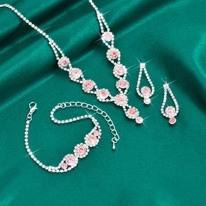 Detailed view of pink crystal necklace earrings and bracelet set on dark green silk