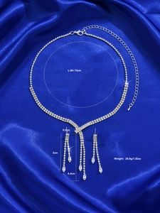 Detail showing dimensions of silver rhinestone necklace and tassel earrings on blue satin