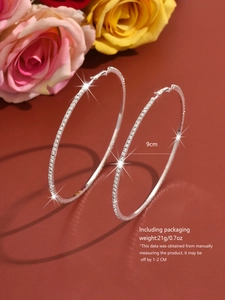 Macro view of 9cm silver hoop earrings with white crystals on a rose background
