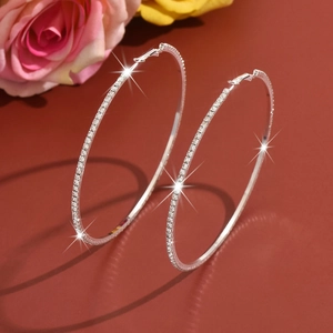 Detailed view of large silver hoop earrings with crystals on a red background