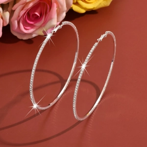 Close-up of silver hoop earrings with white zircons on a classic brown background