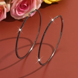 Detailed close-up of large black rhinestone hoop earrings against a warm floral backdrop