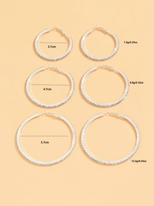 Three pairs of shiny rhinestone hoop earrings in sizes 3.7cm, 4.7cm, and 5.7cm on beige surface