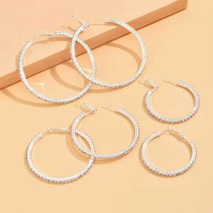 Three pairs of silver crystal hoop earrings in various sizes on an orange background