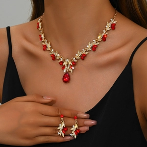 Close-up of bridal jewelry set with red pear-cut crystals and gold vine leaf necklace