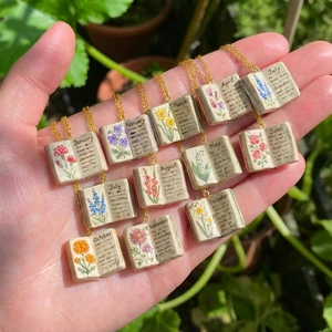 Vista macro di 12 collane a libro con fiori di nascita e dettagli dipinti a mano dei mesi