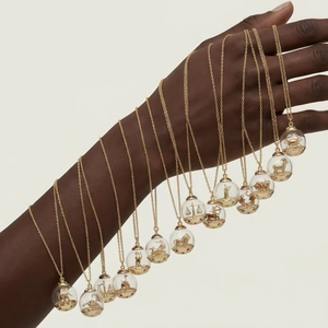 Présentation de 12 colliers zodiacaux dorés avec sphères de verre sur le bras du mannequin