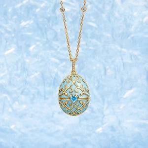 Makroaufnahme des blauen Emaille-Eianhängers mit herzförmigem Stein und Goldranken