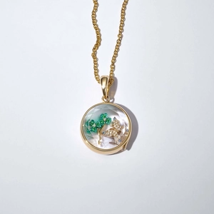 Détail macro du pendentif médaillon doré avec trèfle et papillon sous cristal clair