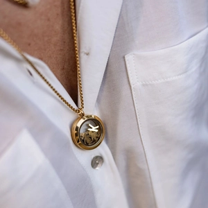 Close-up of golden round locket necklace with K initial and miniature figure charms