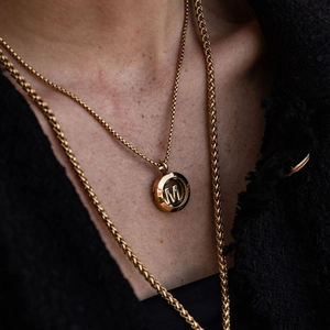 Close-up of a 18k gold initial M locket pendant on a delicate chain for women