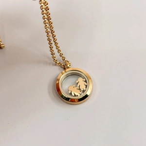 Detail of a 18k gold round glass locket pendant featuring two small metal figures inside