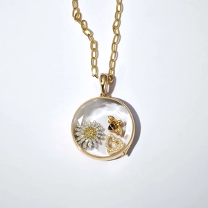 Détail d'un médaillon doré contenant des breloques de marguerite, d'abeille et de cœur