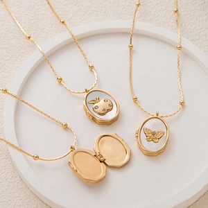 Golden locket necklace with shell inlay and butterfly pendant on stone tray