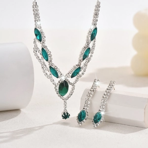 Macro detail of silver necklace and earrings set with green stones on a white stone base