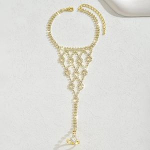 Dettaglio della catena a mano dorata con nappe multistrato e cristalli su sfondo texture