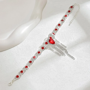 Detalle de tobillera plateada con pedrería roja en forma de gota y flecos brillantes