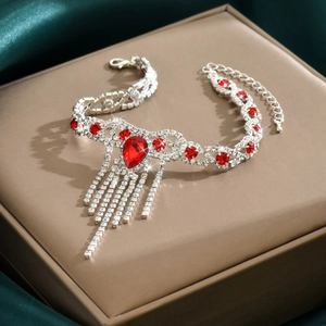 Primer plano de tobillera plateada con pedrería roja en gota y borlas de cristal brillante