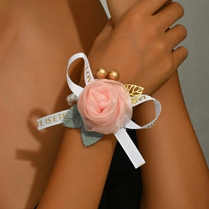 Detail of bridal wrist corsage with pink fabric rose, gold leaves and love ribbon
