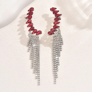 Macro detail of silver tassel earrings with red teardrop stones on stone background
