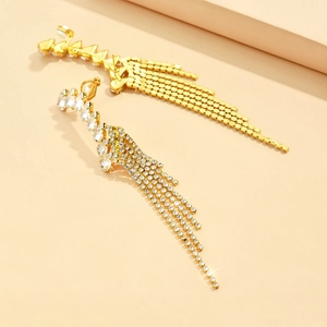 Detail of gold tassel clip-on earrings with shimmering rhinestones on a beige background