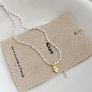 Makro-Detail von Silber-Perlenkette und Gold-Oval-Anhänger mit LOVE-Schriftzug auf Stoff