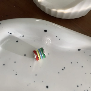 Rainbow enamel cylinder pendant necklace in minimalist style on white porcelain tray