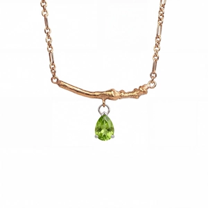 Detailed close-up of a pear-cut green gemstone pendant with a branch-like gold bar design