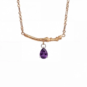 Detail of gold branch bar necklace with a purple teardrop-shaped zircon pendant