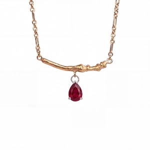 Detailed view of teardrop red zircon necklace with gold branch design on white background