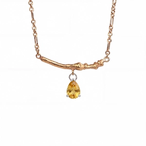 Close-up of golden branch pendant with a pear-cut yellow gemstone on a fine chain