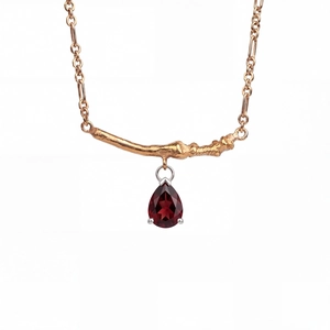 Close-up of pear-cut garnet pendant on a golden branch necklace with fine textures