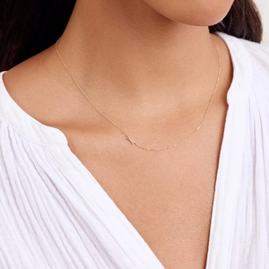 Detail of a minimalist gold necklace with a small X initial pendant worn by a model